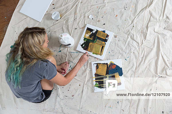 Draufsicht einer Künstlerin  die auf einem Staubblatt kauert und abstrakte Leinwand malt