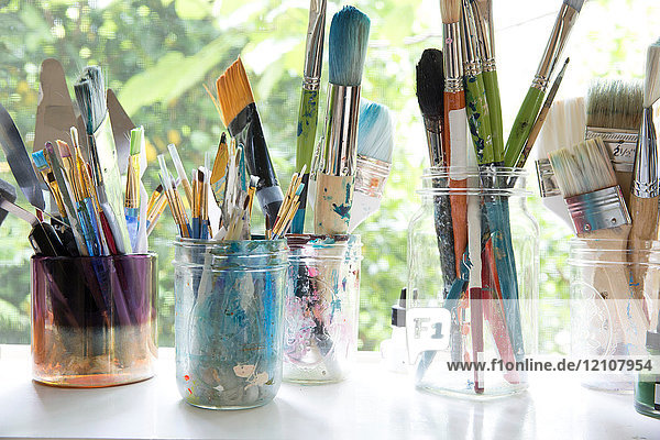 Reihe von Krügen mit verschiedenen Künstlerpinseln auf dem Fensterbrett des Künstlerateliers