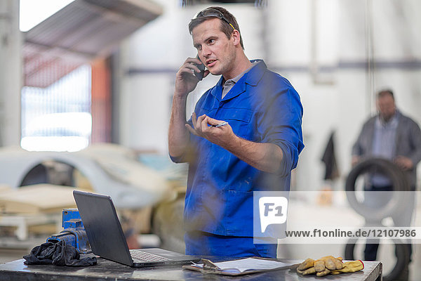 Automechaniker beim Smartphone-Anruf in der Werkstatt