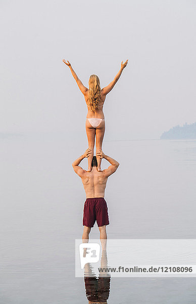Young couple on beach  woman standing on man's shoulders  rear view