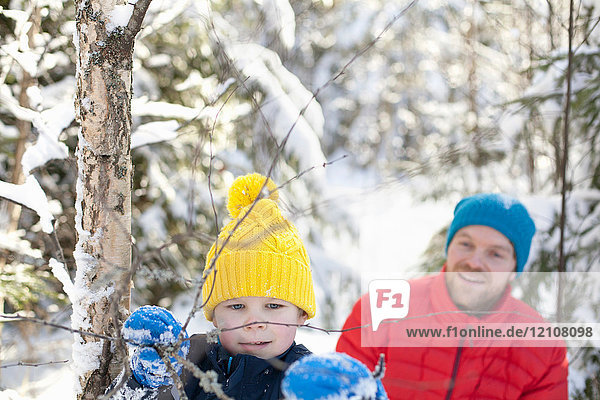 Man and son looking at tree twigs in snow covered forest