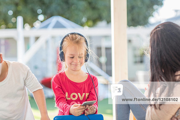 Junges Mädchen hält Smartphone in der Hand und trägt Kopfhörer