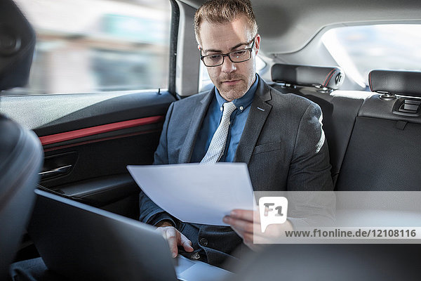 Geschäftsmann sitzt hinten im Auto  benutzt Laptop  hält Dokument