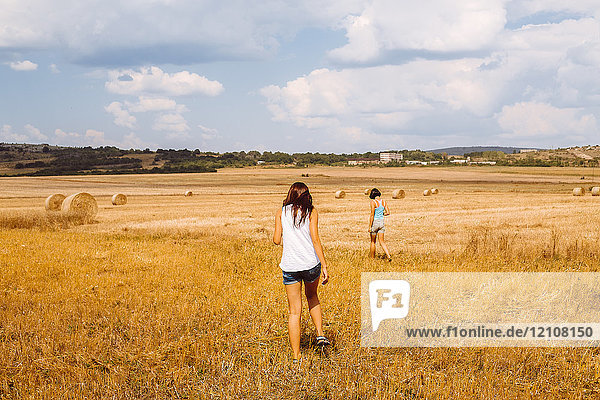 Rear view of women walking in wheat field