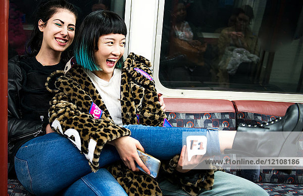 Zwei junge stilvolle Frauen lachen in einem U-Bahnwagen