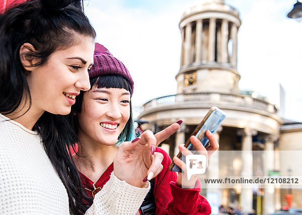 Zwei junge  stilvolle Frauen schauen sich ein Smartphone an  London  UK