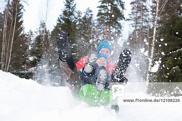 Man and son on speeding toboggan in snow covered forest