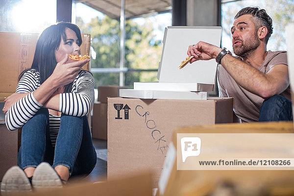 Ehepaar in neuem Zuhause  umgeben von Kartons  beim Pizzaessen