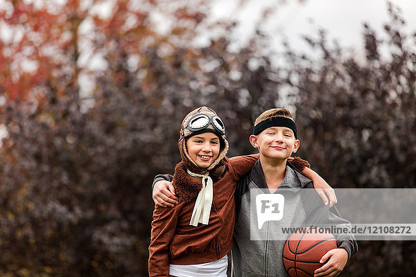 Portrait of girl and twin brother wearing basketball player and pilot costumes for halloween in park