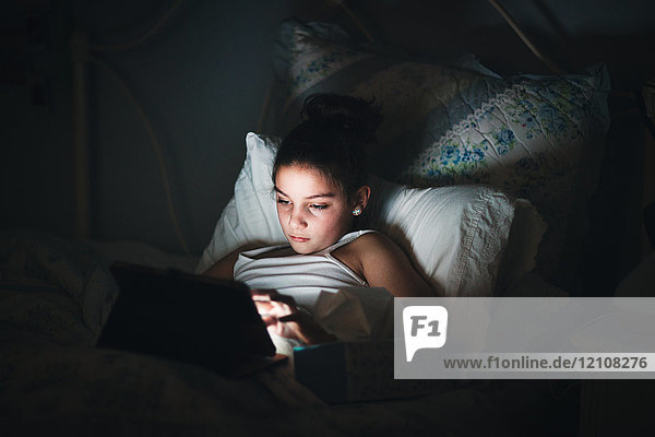 Girl in bed illuminated by light from digital tablet