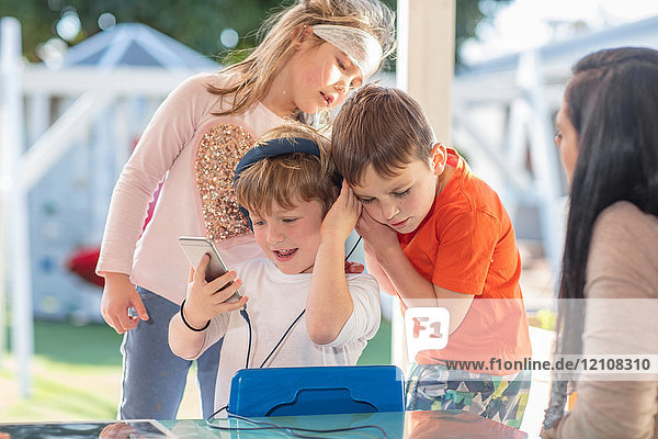 Drei kleine Kinder  die ein Smartphone benutzen und über Kopfhörer hören