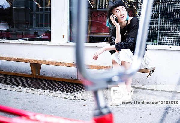 Junge elegante Frau sitzt vor einem Geschäft und telefoniert mit einem Smartphone