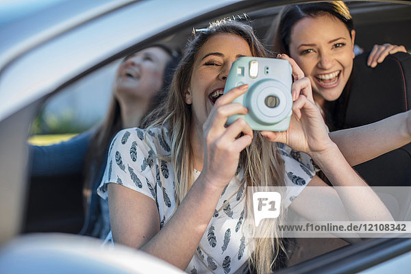 Junge Frau im Auto mit zwei Freunden  die aus dem Autofenster fotografiert