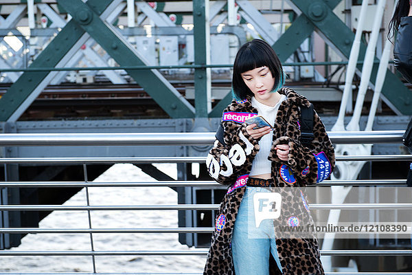 Stilvolle junge Frau betrachtet Smartphone auf der Millennium Footbridge  London  UK