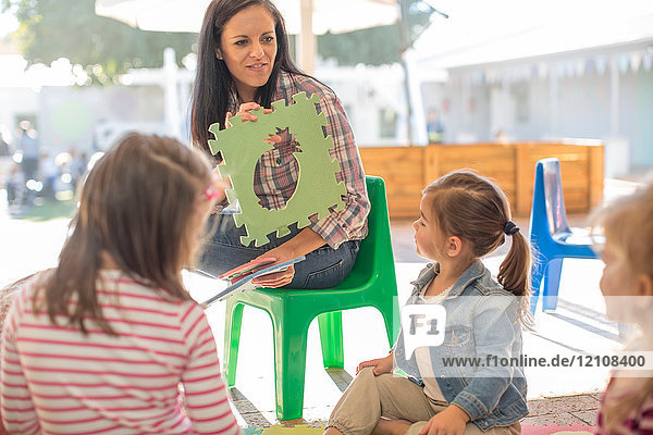 Mittelgroße erwachsene Frau  die mit einer Gruppe von Kindern sitzt und ihnen die Form von Schaumstoff zeigt