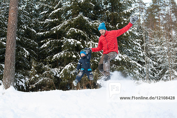 Man and son jumping from snow covered forest hill