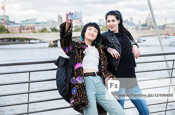 Two young stylish women taking smartphone selfie on millennium footbridge  London  UK
