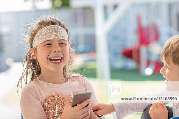 Junges Mädchen hält Smartphone in der Hand  trägt Kopfhörer  lacht