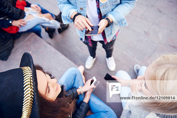Draufsicht auf junge erwachsene Freunde  die auf Smartphones schauen und sich auf Stadttreppen unterhalten