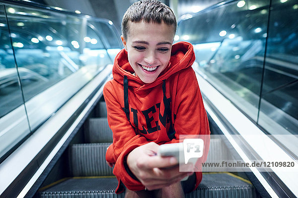 Kurzhaarige junge Frau fährt die Rolltreppe der U-Bahn-Station hinunter und schaut auf ein Smartphone