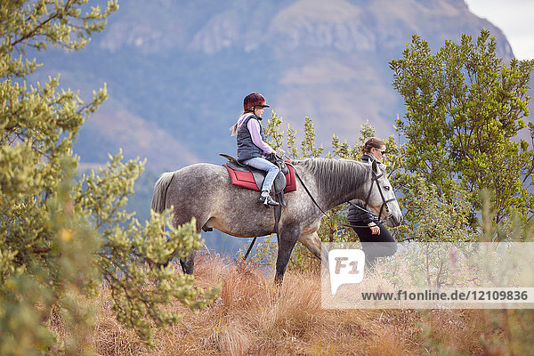 Mädchen reitet Pferd in ländlicher Umgebung  die Mutter geht an ihrer Seite