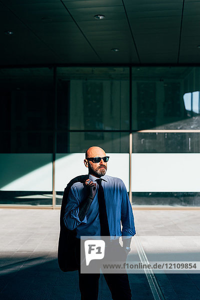 Porträt eines reifen Geschäftsmannes  der im Freien steht und eine Anzugsjacke über der Schulter trägt