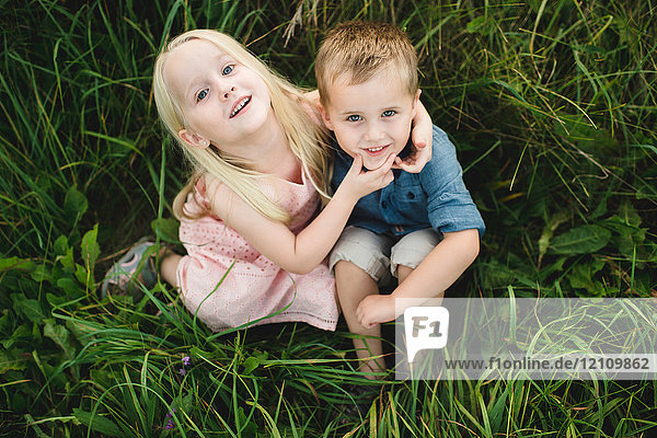 Junge und Mädchen sitzen zusammen im hohen Gras und schauen in die Kamera