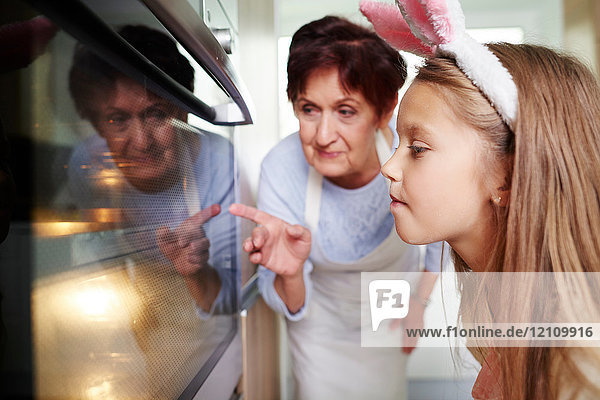 Mädchen und Großmutter schauen sich Osterkekse im Küchenofen an