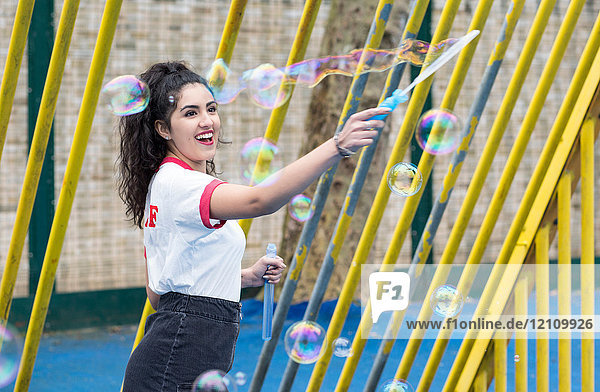 Begeisterte junge Frau auf dem Spielplatz beim Blasenmachen mit dem Blasenzauberstab