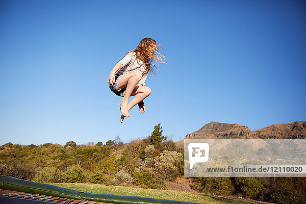 Junges Mädchen springt auf Trampolin  in der Luft  in ländlicher Umgebung