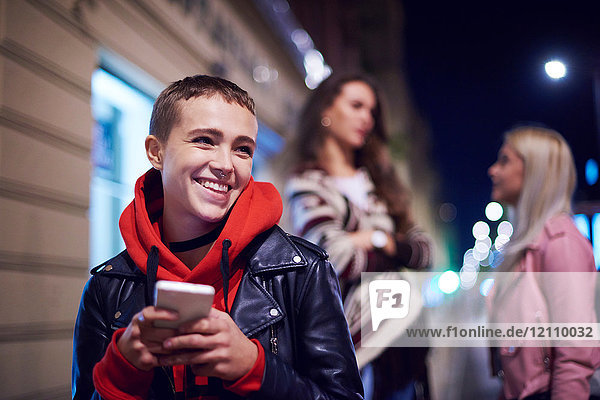 Junge Frau mit Smartphone lacht nachts auf der Straße in der Stadt