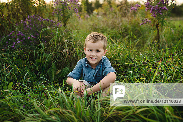 Porträt eines lächelnden Jungen  der im hohen Gras sitzt und in die Kamera schaut
