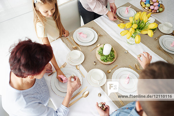 Overhead view of grandmother and family preparing easter dining table