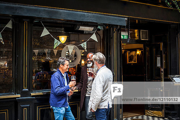 Three mature men  standing outside pub  holding beer glasses  laughing