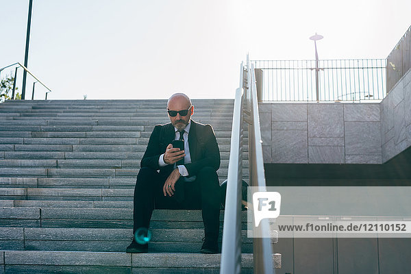 Reifer Geschäftsmann auf Stufen sitzend  mit Smartphone  niedriger Blickwinkel