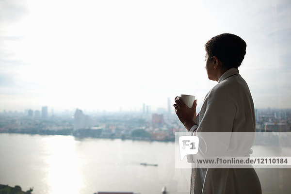 Frau im Bademantel hält Tasse mit Blick auf die Stadt  Bangkok  Krung Thep  Thailand  Asien