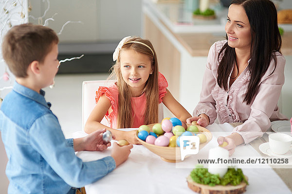Girl with brother and mother preparing colourful easter eggs at dining table