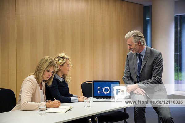 Colleagues in conference room having meeting  using laptop