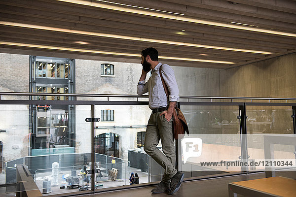 Mann im Hochparterre eines Bürogebäudes telefoniert mit Smartphone