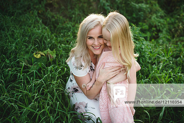 Mutter und Tochter im hohen Gras schauen lächelnd in die Kamera