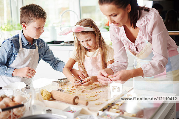 Girl  brother and mother baking easter biscuits at kitchen counter