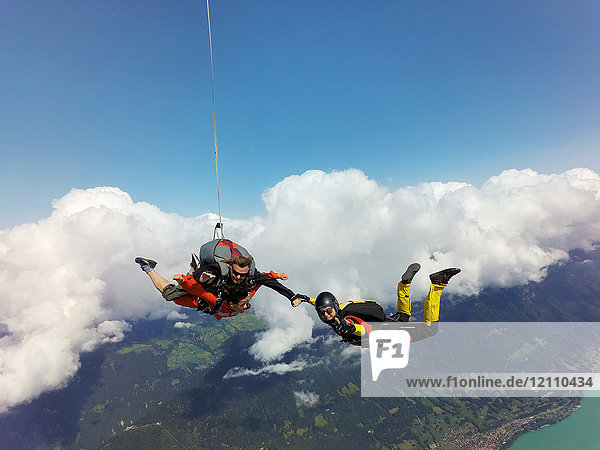 Porträt von Tandemfallschirmspringern  die mit der Fallschirmspringerin über Wolken und Landschaft Händchen halten