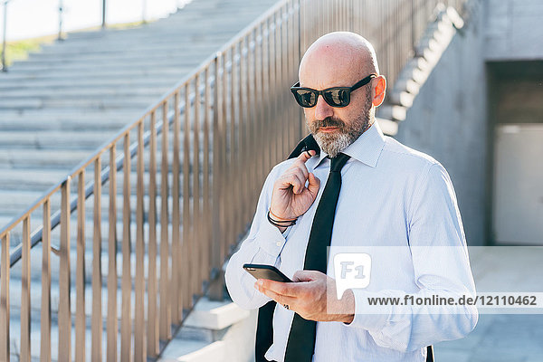 Älterer Geschäftsmann im Freien  Jacke über der Schulter tragend  Smartphone benutzen