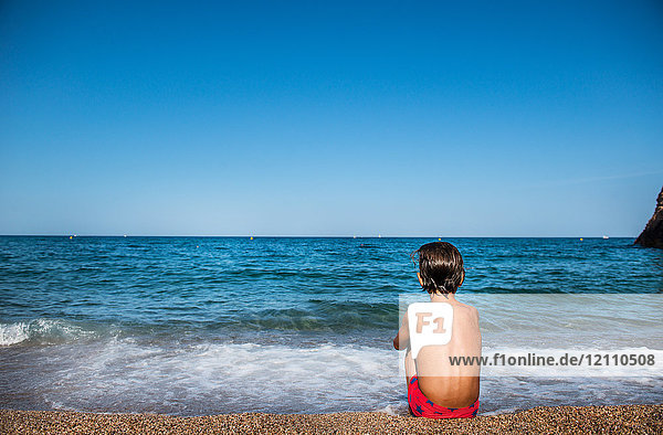 Rückansicht eines am Strand sitzenden Jungen mit Blick aufs Meer  Begur  Katalonien  Spanien