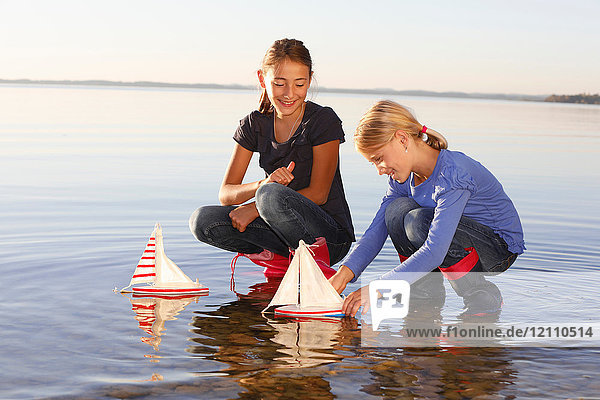 Two young girls floating toy boats on water