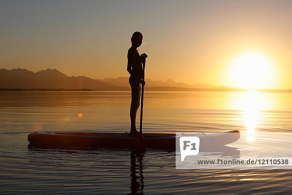 Young girl paddle boarding on water  at sunset