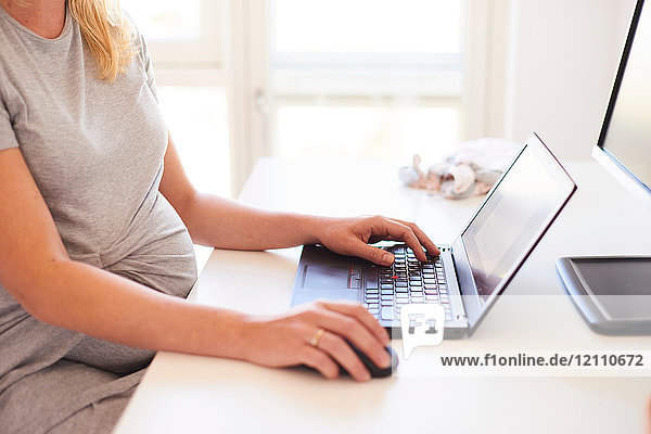Cropped shot of pregnant young woman at desk typing on laptop