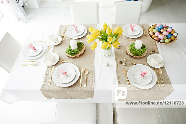 Hasenohrservietten und Schale mit bunten Ostereiern auf dem Esstisch