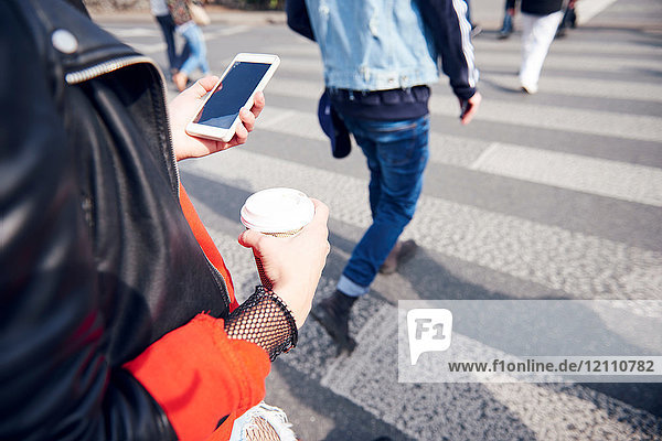Person on pedestrian crossing with coffee and smartphone