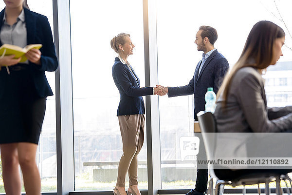 Businesswoman and man shaking hands by office window